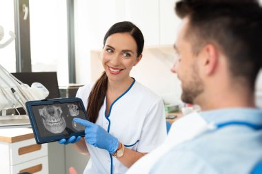 Klinikte diş muayenesi. Diş hekimi dijital tablet ekranda diş röntgeni gösteriyor. 3D tomografi teknolojisi.
