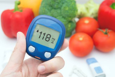 Adamın elinde kan şekeri ölçer ve bir sürü sebze var. Taksimetre 118 mg / dl gösteriyor.