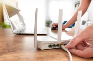 Modern Wi-Fi yönlendiricisini oturma odasındaki ışıklı masaya bağlayan kişi