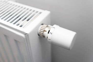 Kişi radyatörün sıcaklığını ayarlıyor. Radyatör beyaz ve üzerinde düğmesi var.