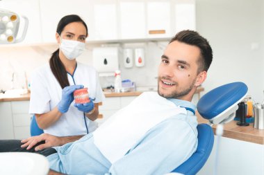 Diş hekimi, dişçide bir hastanın dişlerini muayene ediyor. Çene modeli.