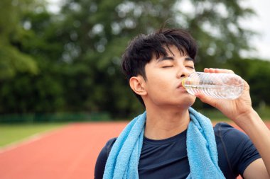 Parkta fotokopi odasıyla koştuktan sonra şişeden su içen genç Asyalı gençleri kapatın. Fitness erkek profili açık hava, spor ve rahatlama kavramı