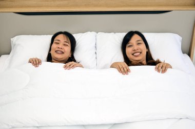 Mutlu Dostluklar: Beyaz yatakta uzanan, gülümseyen ve eğlenen iki kadın