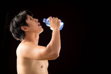Rahatlatıcı Spor Molası: Üstsüz Asyalı Sporcu elinde şişe tutuyor ve Büyüleyici Siyah Arkaplan 'da fotokopi alanı ile su içiyor