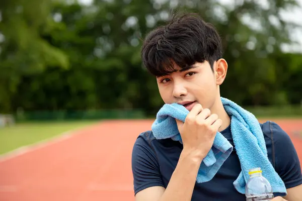 One Asia male Athlete use towel wipe face and Drinking Water Bottle on the Track with copy space; Mineral Water Stay Active and Hydrated Break