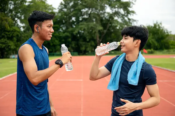 Two Asia male Athlete Drinking from a Water Bottle on Track together; Mineral Water Stay Active and Hydrated Break