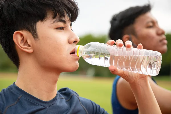 Two Asia male Athlete Drinking from a Water Bottle on the Track together; Mineral Water Stay Active and Hydrated Break