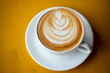 Kapuçino ya da yapraklı köpüklü latte, kahve temiz fincan yakın çekim. Portakallı ahşap masa arkaplanlı içecek.