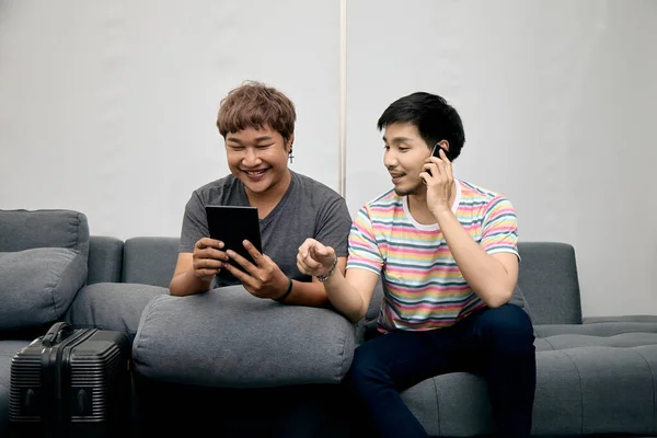 LGBT Couple Engaging in Digital Communication While Lounging Comfortably: A Relaxed, Tech-Savvy Scene in a Cozy Home Setting