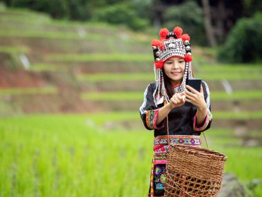 Bu portre, geleneksel giysiler içinde Asyalı bir Hmong hanımı yakalıyor, pirinç tarlasının yeşil boşluğunda dururken cep telefonu ekranına bastırıyor, modern teknolojinin geleneksel yaşam tarzlarıyla kusursuz bütünleşmesini simgeliyor.