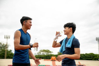 İki genç Asyalı atletik arkadaş atletizm antrenmanlarında susuz kalıp iyi huylu bir kahkaha atıyorlar.