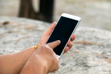 Son sınıf öğrencisinin akıllı telefonuyla etkileşim kurduğu, dokunmatik ekrana odaklandığı, açık havada parkta çekilmiş görüntüleri.