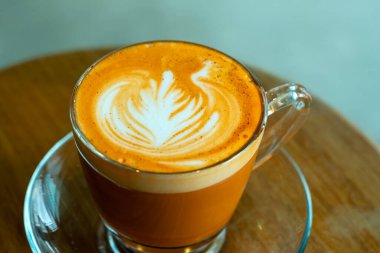 Cam fincana yakın kahve, güzel latte sanatıyla, ahşap masadaki cam tabakta servis edilir.