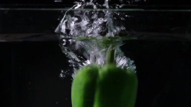 Yeşil çan biberinin hareket bulanıklığı ve suya sıçraması dinamik sıçramalar ve baloncuklar ile karanlık bir arkaplanda