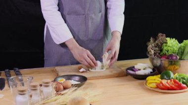 Genç aşçı, mutfak tezgahında taze sebze, malzeme ve baharatla haşlanmış yumurta dilimliyor.