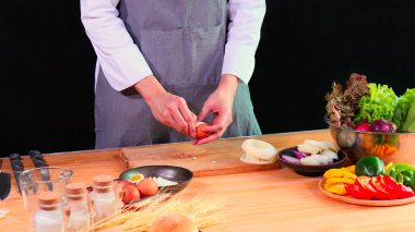 Gri önlüklü genç aşçı, taze sebze ve malzemelerle çevrili ahşap kesme tahtasıyla haşlanmış yumurtayı kaseye koyar.