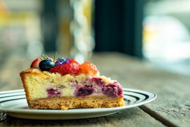 Taze böğürtlenlerle kaplı, tabakta servis edilen, kırsal ahşap masaya yerleştirilmiş bir dilim cheesecake.