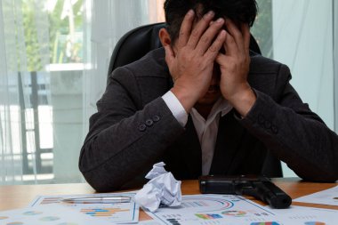 Ekonomik dökümanlar ve tabancalarla çevrili, stresli bir iş adamı krizi resmediyor.