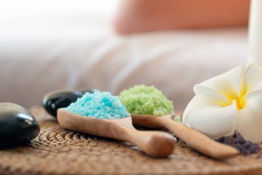 Renkli aromaterapi tuzları ve dokunmuş mindere yerleştirilmiş tesisat çiçekleri, rahatlama ve spa atmosferini çağrıştırıyor.