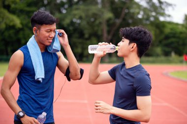 İki genç adam antrenmandan sonra dinleniyor, su içiyorlar ve serinliyorlar.