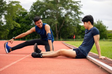 İki genç sporcu antrenmandan sonra esneklik ve gevşemeye odaklanarak koşu pistinde esniyorlar.