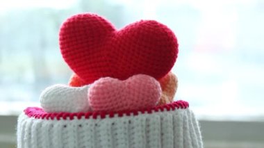 Kırmızı, pembe ve beyaz işlemeli renkli kalplerin yakın plan görüntüsü örülmüş bir sepete yerleştirilmiş arka planda yumuşak doğal ışık ile dönen bir hareket.