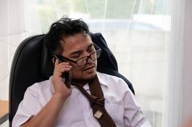 Darmadağın kıyafetlerle çalışan yorgun bir ofis çalışanı cep telefonuyla konuşuyor, iş günü stresli ve bunalmış görünüyor.