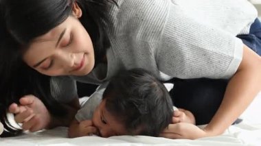 Annenin yatakta oynarken gülen bebeği öptüğü neşeli an, evde neşeli aile zamanı boyunca yakın bağ ve duygusal bağ.