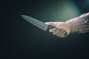Yakın çekim erkek eli keskin mutfak bıçağını siyah arka planda düşük ışıkta yatay olarak tutuyor.