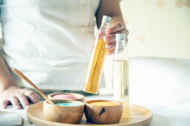 Bir spa terapisti, ahşap bir tepsinin üzerinde renkli önlüklerle gerekli bir yağ şişesini tutar ve rahatlama tedavisine hazırlanır.