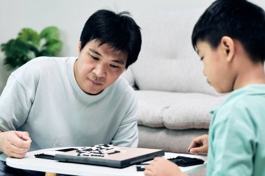 Asyalı baba ve oğul evde bir masa oyunu oynarken konsantre olup stratejik düşünme becerilerini geliştiriyorlar.
