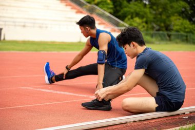 Eğitimden önce iki erkek sporcu, esneklik ve hazırlık üzerine yoğunlaşarak kırmızı pist üzerinde ısınıyorlar.