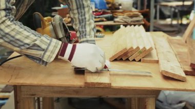 Eldivenli ellerin yakın çekimi atölyedeki marangozluk bankında tahta kalemi kalem ve cetvelle işaretliyor.