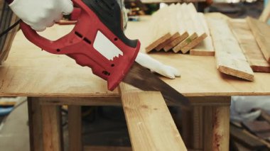 Eldivenli eldiven, kırmızı elektrikli testereyle marangoz tezgahında tahta kesmek için kullanılıyor.