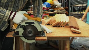 Marangoz, eldiven ve koruyucu maske takarken tezgahta dairesel testereyle tahta kesiyor.