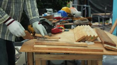 Marangoz, eldiven ve güvenlik maskesi takarken tezgahta yuvarlak testereyle tahta kesiyor.