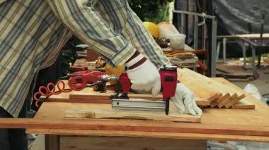 Marangoz koruyucu eldiven ve kulaklık takarken tezgahtaki odunları takmak için kırmızı çivi tabancası kullanıyor.