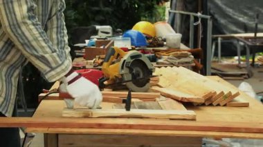 Marangoz elinin eldiven giyip, atölyedeki ahşap tahtayı tutturmak için kırmızı çivi tabancası kullanmasını.