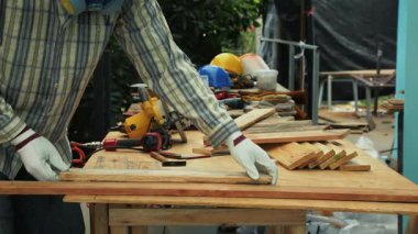 Marangoz eldiven takıyor atölyedeki tezgahta farklı boyutlarda tahta diziyor.
