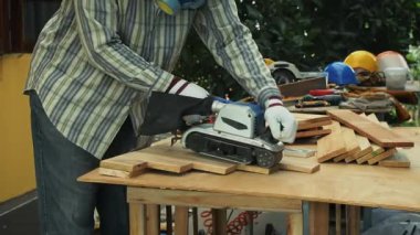 Marangoz elektrikli kemer zımpara makinesi kullanıyor. Açık hava tezgahındaki ahşap tahtaları düzleştirmek için.