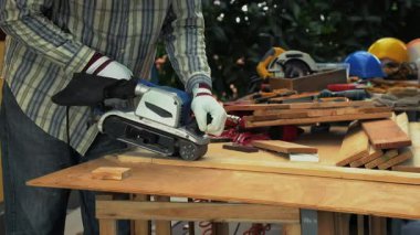 Eldiven takan işçiler ahşap tahta zımpara ve elektrikli kemer zımpara ile dış tezgahta çalışırlar.