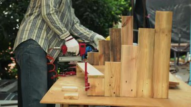 Marangoz, eldiven ve çizgili tişört giyerken tezgahta çivi tabancasıyla ahşap tahtalar monte ediyor.