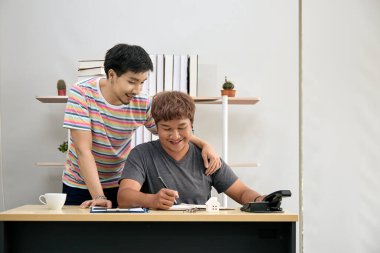 Küçük bir ev modeli ve anahtarla evrak işlerini halleden mutlu çift, emlak alımını veya anlaşmayı sembolize ediyor.