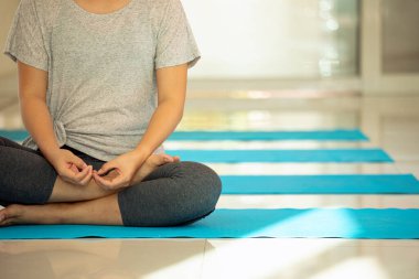 Nilüfer pozisyonunda oturmuş, kapalı alanda meditasyon yapan, mavi yoga minderleri huzurlu bir stüdyoda hizalanmış bir kadının yakın çekimi.