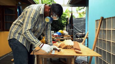 Koruyucu gözlük takan ve maske takan bir marangoz tezgahın üzerindeki ahşap kalası ölçer, kesin kesim ve ahşap işçiliğine hazırlanır.