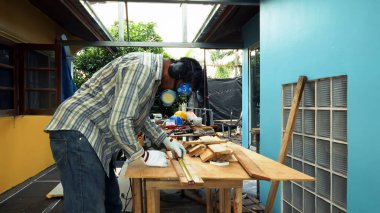 Güvenlik teçhizatı takan bir adam ahşap bir tahtayı mezura ile ölçer, ahşap işçiliği ya da inşaat için malzeme hazırlar.