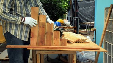 Eldiven takan kişi tezgahta tahta keser, marangozluk çalışma alanında basamaklı ahşap bir yapı inşa eder.