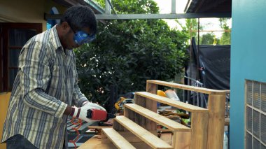 Güvenlik teçhizatı içinde bir marangoz, açık hava atölyesinde ahşap bir merdiveni monte ederken montajlı çivi tabancasıyla çalışır.