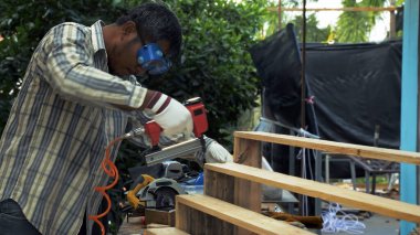 Güvenlik gözlüğü ve eldiven takan bir marangoz, tahta merdiven inşa ederken tahta kalasları güvence altına almak için pnömatik çivi tabancası kullanır.