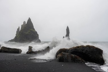 Siyah kumsal Reynisfjara ve Reynisdrangar - İzlanda 'nın güneyindeki Vk Mrdal köyü yakınlarındaki Reynisfjall Dağı' nın altında yer alan bazalt deniz yığınları